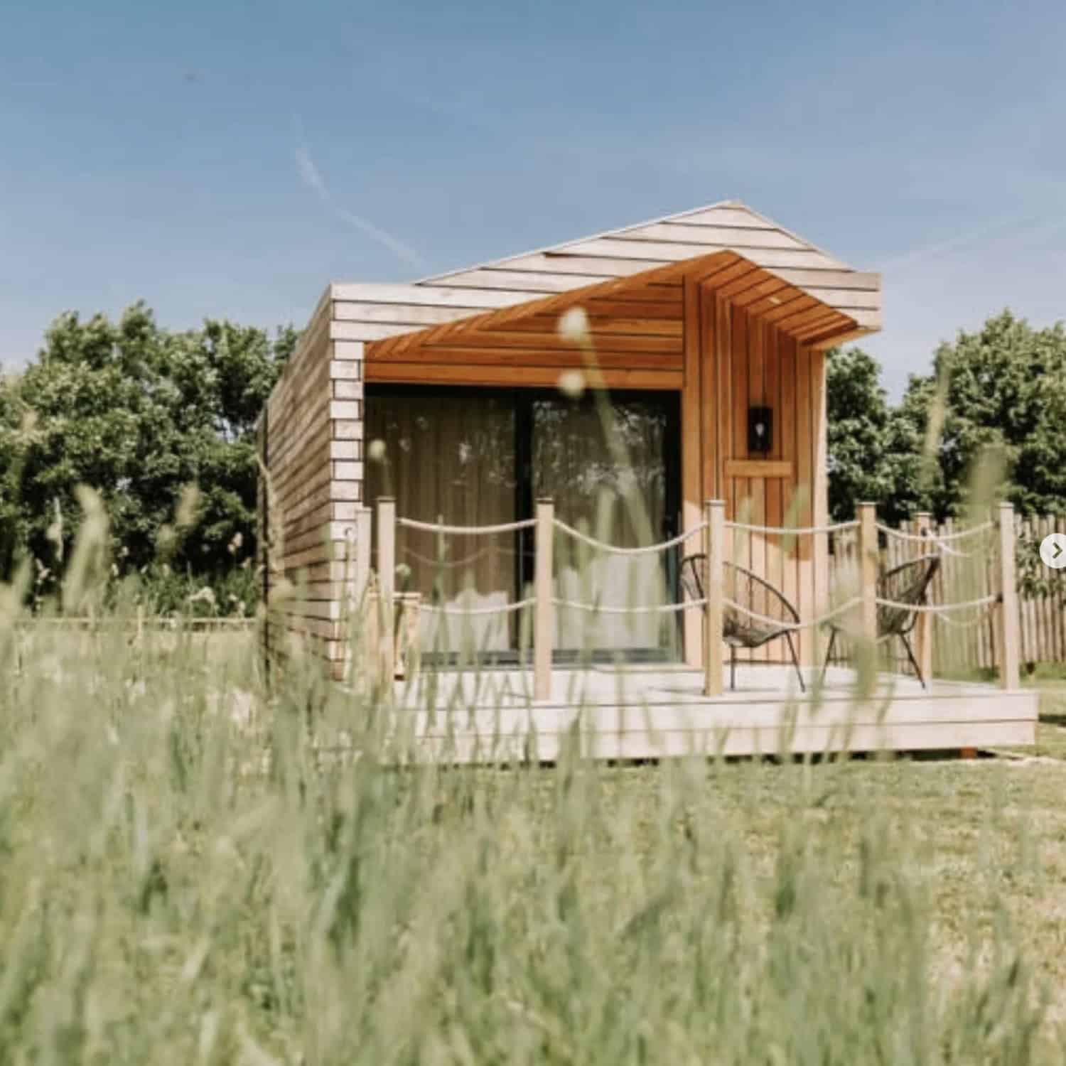 Modern wooden tiny house cabin with deck in meadow